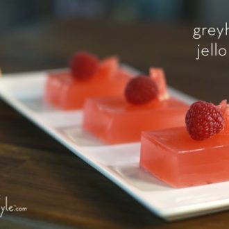Three Jello shots made from ruby red grapefruit juice and topped with raspberries.