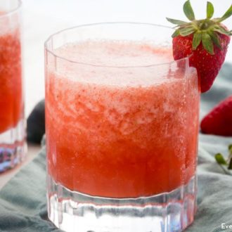 Two delicious glasses of strawberry and orange vodka slush, garnished with fresh strawberries.