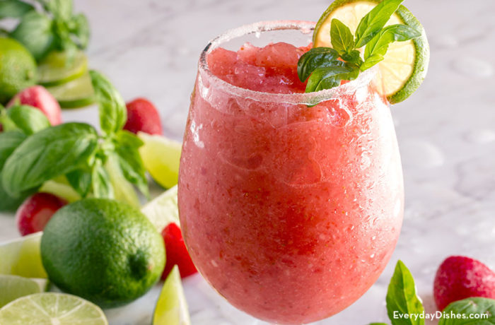 A glass of a delightfully refreshing strawberry basil daiquiri garnished with basil and a slice of lime.