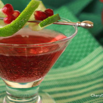 A glass with a refreshing vodka pomegranate cocktail with a lime garnish.