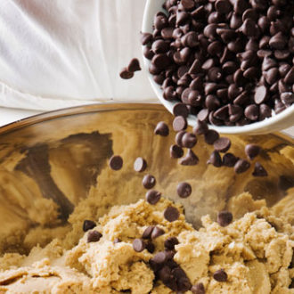 A batch of cookie dough with chocolate chips being poured into it.