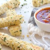 A batch of homemade baked panko-crusted mozzarella sticks with a side of dipping sauce.
