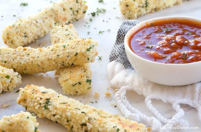 A batch of homemade baked panko-crusted mozzarella sticks with a side of dipping sauce.