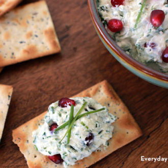 Goat cheese pomegranate dip with fresh herbs, spread onto a cracker.