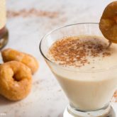 A delicious eggnog martini garnished with a mini donut and sprinkled with cinnamon.