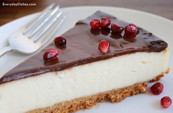 A slice of homemade cheesecake with chocolate ganache and pomegranate seeds.