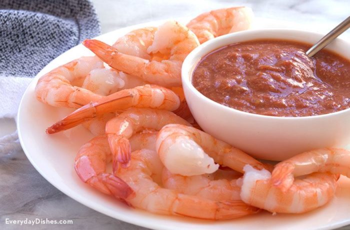 A plate of delicious shrimp with a bowl of spicy cocktail sauce.