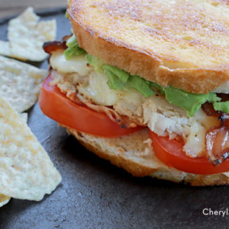 A quick and easy bacon turkey avocado melt, ready to enjoy with chips.