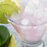 A glass full of delicious pink lemonade margarita garnished with a lemon and a lime