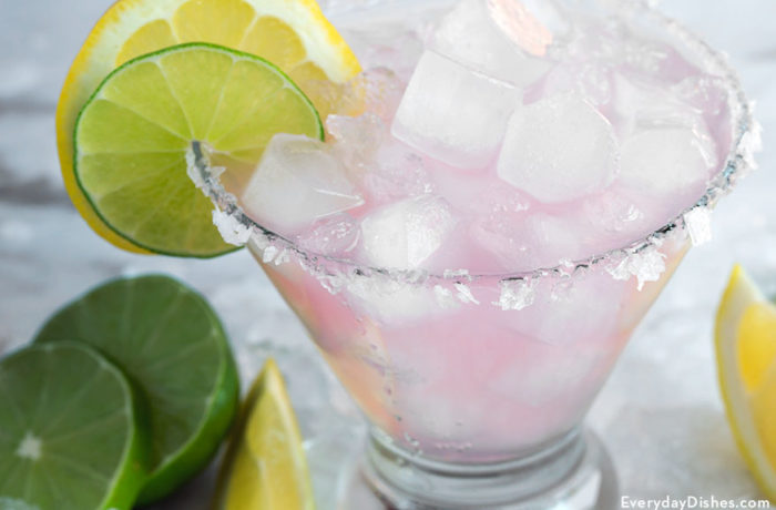A glass full of delicious pink lemonade margarita garnished with a lemon and a lime