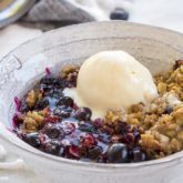 A bowl with a serving of homemade blueberry crisp that's topped with ice cream.