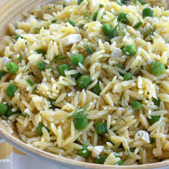 A bowl full of lemon orzo salad with sweet peas and feta cheese, ready to serve.