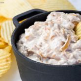 A dish of homemade French onion dip with a chip dunked in it.