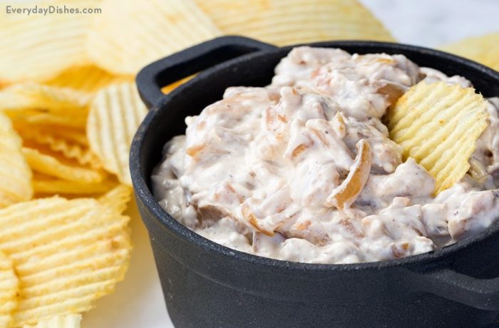 A dish of homemade French onion dip with a chip dunked in it.
