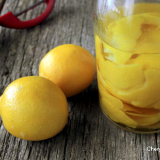 A bottle of homemade lemon extract next to two whole lemons.