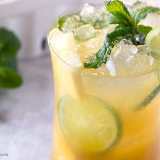 A glass of refreshing pineapple fizz cocktail, garnished with mint and lime.