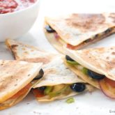 A freshly made veggie quesadilla, sliced up into portions next to a bowl of salsa.