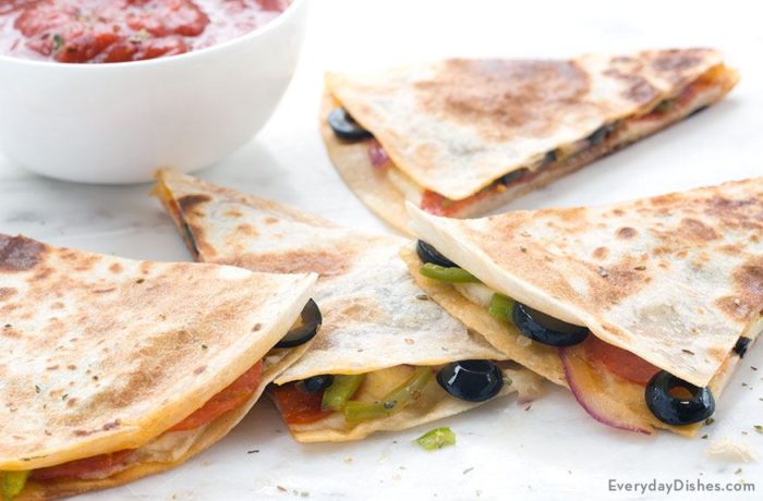 A freshly made veggie quesadilla, sliced up into portions next to a bowl of salsa.