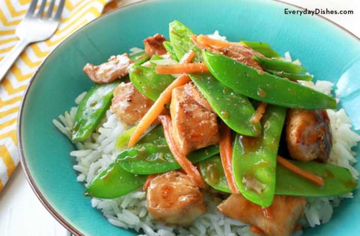 Sauteed chicken and snow peas, served on a plate over rice.