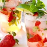 Two resfreshing glasses of summertime strawberry mojitos that are garnished with mint and limes.