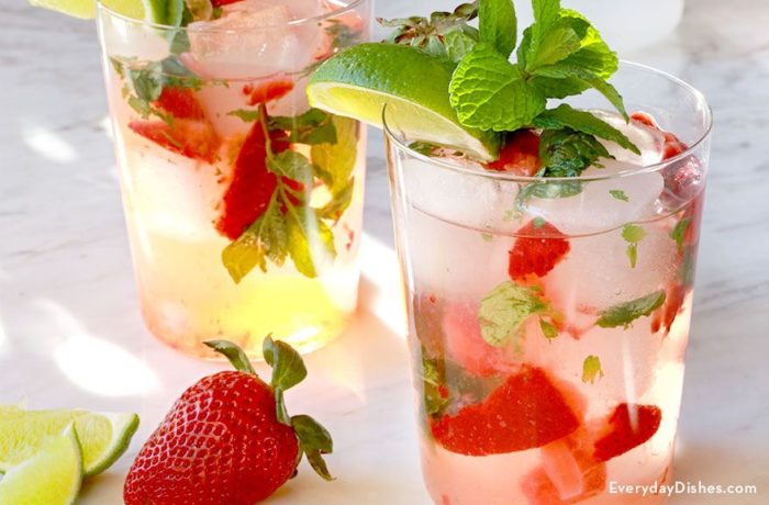 Two resfreshing glasses of summertime strawberry mojitos that are garnished with mint and limes.