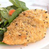 A plate with a serving of baked quinoa-crusted chicken served for dinner with a side salad.