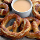 Homemade soft pretzels, surrounding a bowl of dipping sauce.