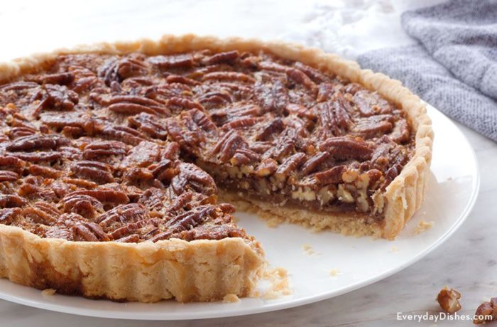 A freshly made pecan pie tart with a slice cut out of it.
