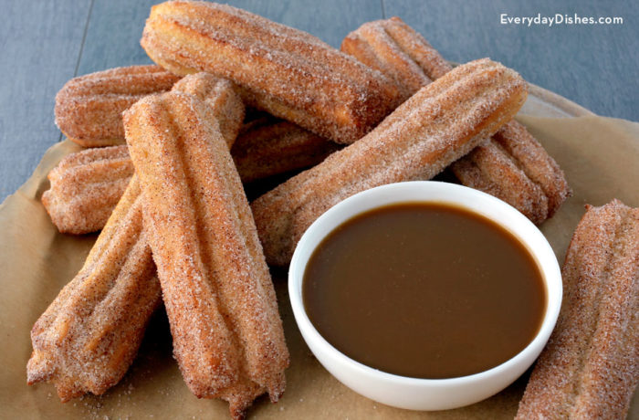 A homemade batch of baked churros, with a bowl of dipping sauce.