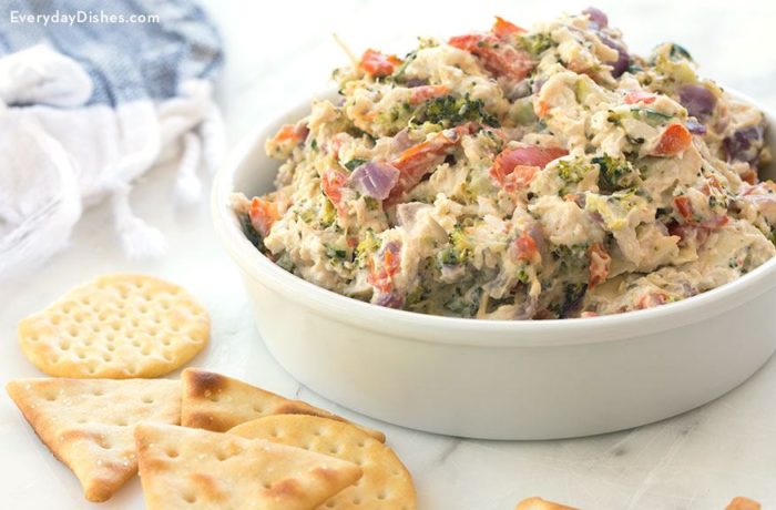 A bowl full of chicken spread with roasted vegetables, served with crackers.