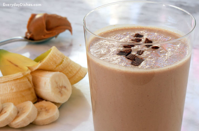 A glass full of a chocolate peanut butter hangover smoothie, topped with chocolate and next to a sliced banana.