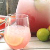 A glass full of a pink limeade margarita next to a pitcher of it