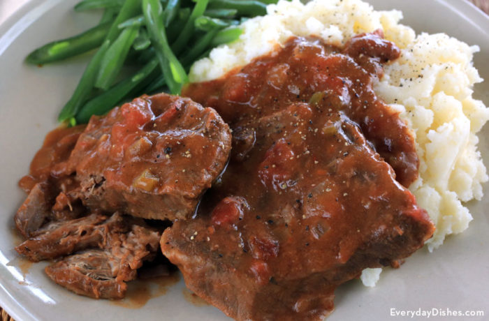 A plate of a delicious slow cooker Swiss steak served with mashed potatoes and green beans.