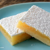 Homemade tangy lemon bars, topped with powdered sugar, sitting on a plate.