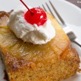 A slice of carrot pineapple upside down cake topped with whipped cream and a cherry.
