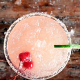 A glass full of a delicious cherry beer margarita, garnished with cherries and lime.