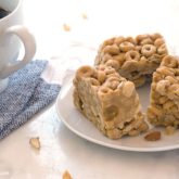 A trio of peanut butter cereal bars on a plate and next to a mug of coffee.
