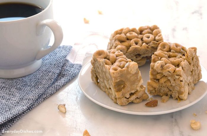 A trio of peanut butter cereal bars on a plate and next to a mug of coffee.
