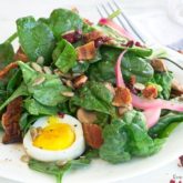 A plate of delicious spinach salad with warm bacon dressing that's ready to enjoy.