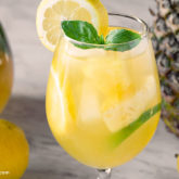 A glass full of a citrus pineapple sangria, garnished with mint and lemon