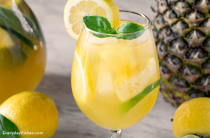 A glass full of a citrus pineapple sangria, garnished with mint and lemon