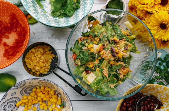 A bowl of a tex mex chicken salad with bowls of different toppings.