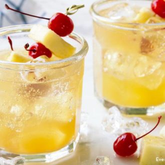 Two glasses of pineapple fizz vodka cocktails, garnished with cherries and pineapple.