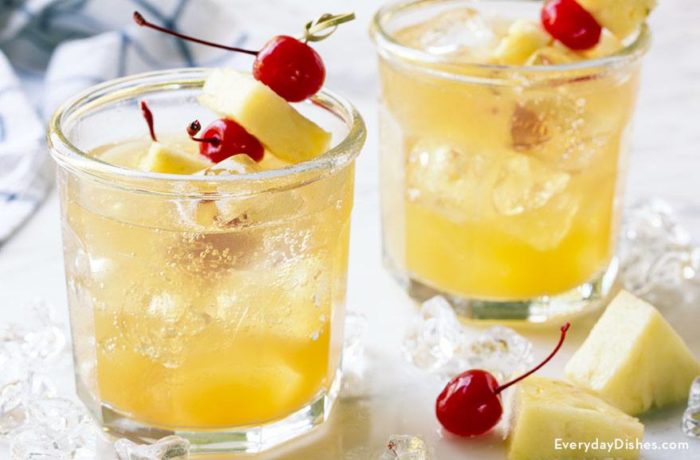 Two glasses of pineapple fizz vodka cocktails, garnished with cherries and pineapple.
