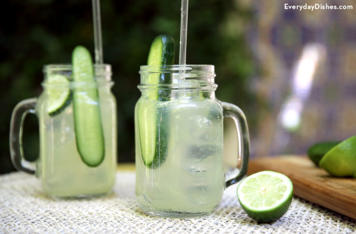Two vodka cucumber limeade cocktails, in mason jar glasses, garnished with cucumber and lime