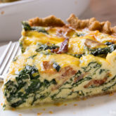 A piece of bacon spinach quiche that's on a plate and ready to eat for dinner.