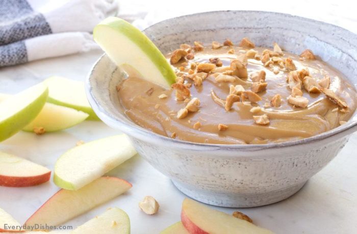 A bowl of caramel dip and apple slices to dunk in it.