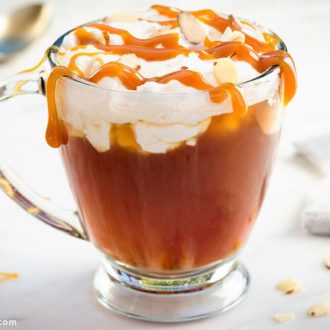 A delicious mug of hazelnut chai tea cocktail, topped with whipped cream and drizzled with caramel sauce.