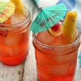 Two mason jars full of a delicious cinnamon mai tai cocktail, garnished with fresh fruit and little umbrellas.