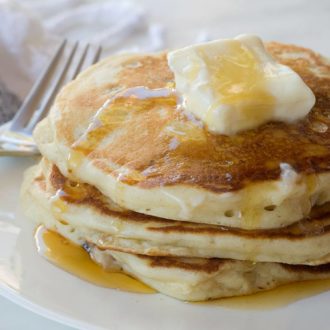 A short stack of fluffy homemade pancakes, topped with butter and syrup.